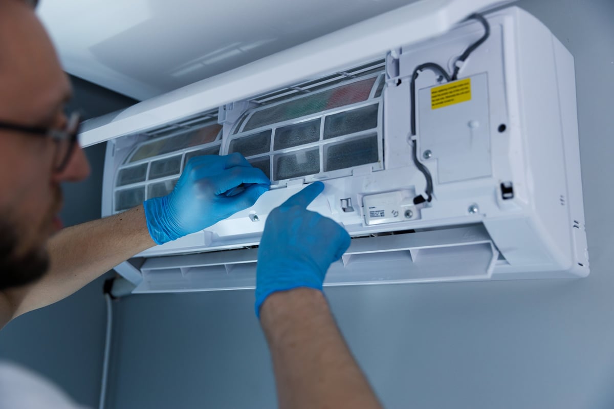 An experienced technician wearing blue gloves is inspecting and cleaning the filter of a split air conditioning unit on the wall, ensuring it operates efficiently in a home environment.
