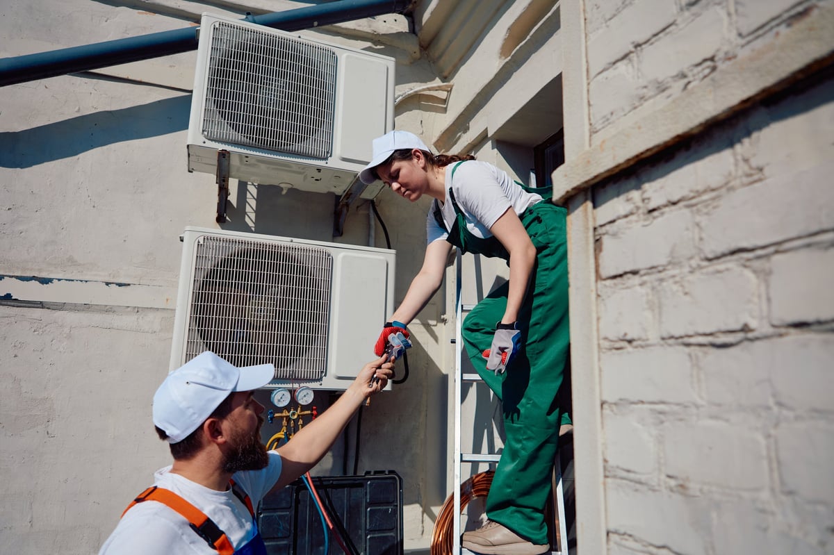 Technicians setting up air conditioning system on building exterior. Concept of technician teamwork, rooftop AC inspection, ladder access maintenance, field service dynamics.
