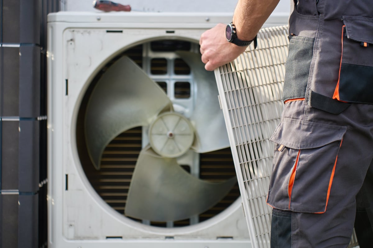 Technician removing front cover grille from outdoor heat pump unit during residential HVAC service