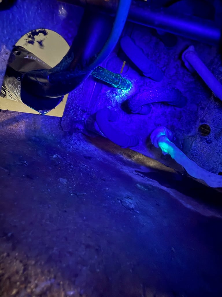 Car undercarriage illuminated with blue UV light, showing grime, oil residue, and chassis components in detail