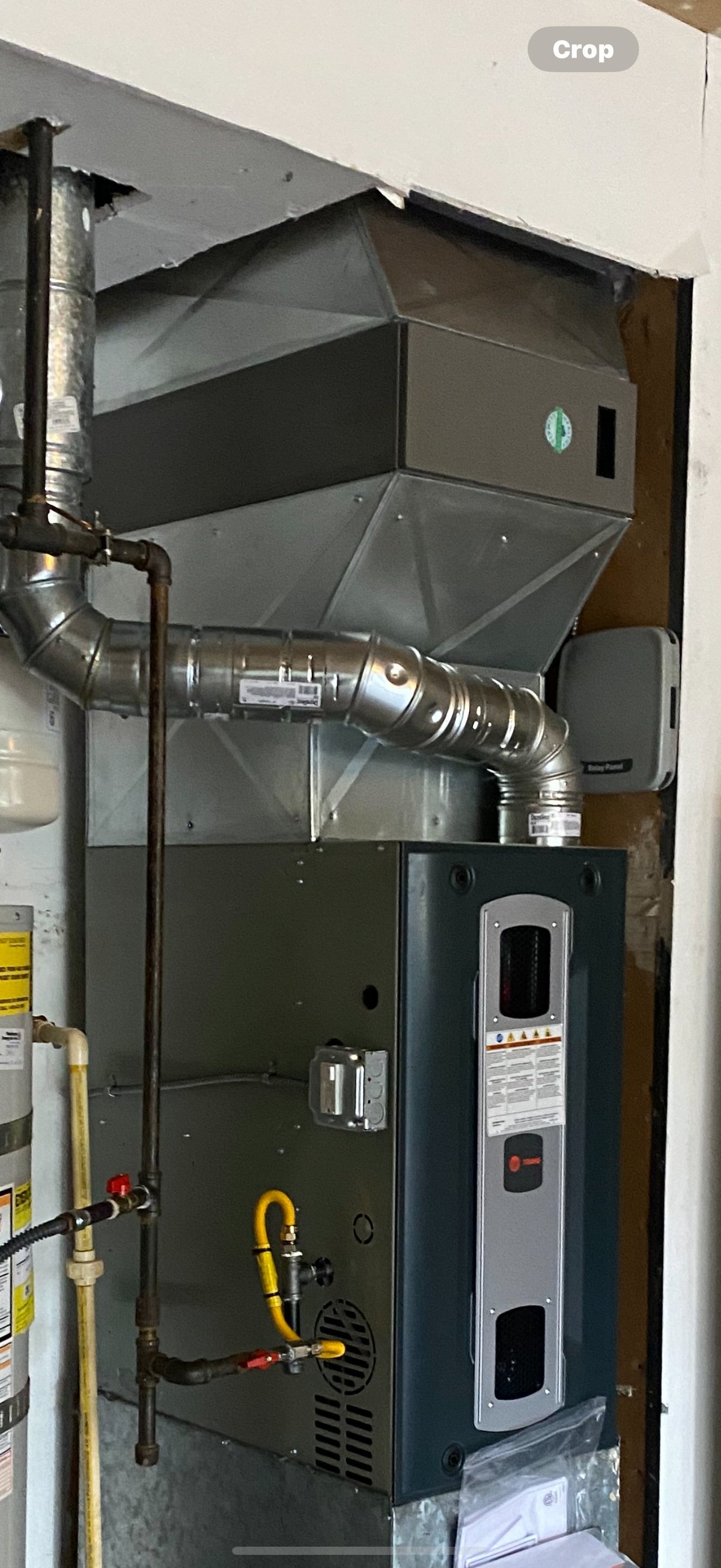 HVAC system installation showing furnace unit with ductwork and metal piping connections in a residential interior wall