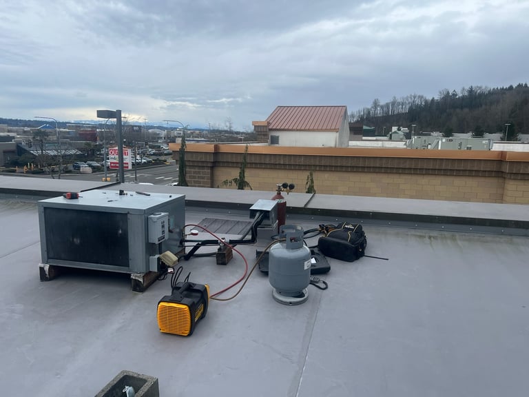Construction workers on a commercial flat roof with HVAC equipment and yellow electrical boxes during installation work