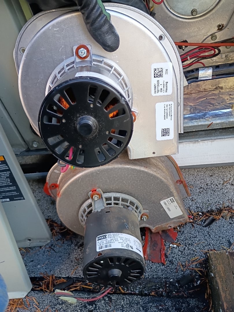 Two HVAC inducer motors stacked vertically with white wire covers, showing black fan wheels and red wiring connections