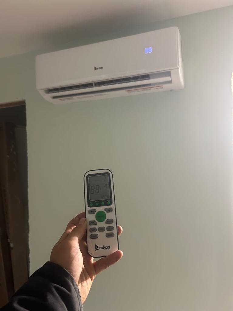 Person holding air conditioner remote control with wall-mounted AC unit displaying blue temperature display above