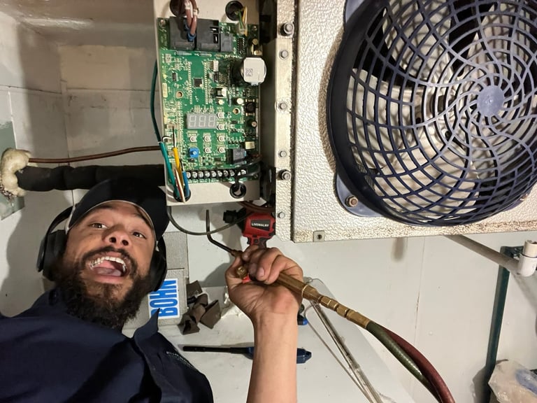 Technician smiling while servicing HVAC system with exposed circuit board and fan unit on wall