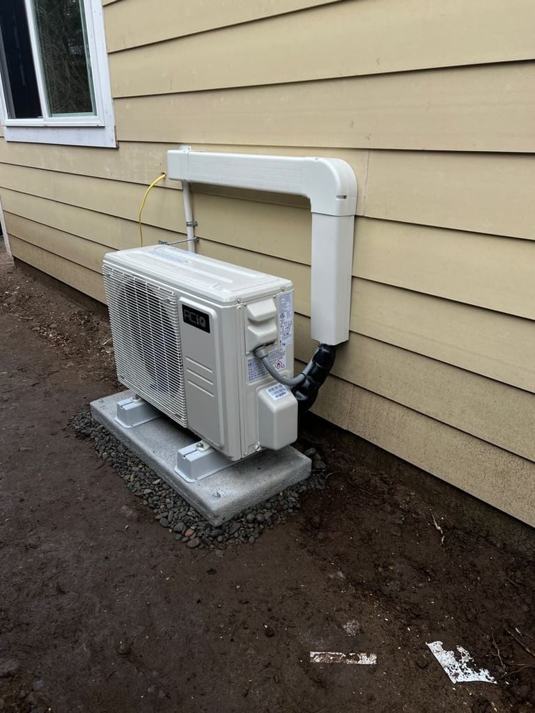 White outdoor air conditioning unit installed on concrete pad against beige siding of house with white PVC pipe connection running up the wall