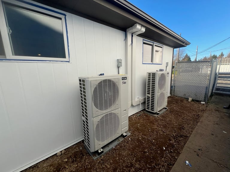 White exterior AC units mounted on side of mobile home with metal fencing and dirt yard